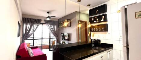 A modern kitchen with a black countertop, white cabinets, and a built-in oven. There is a red sofa in the adjacent living area, and a ceiling fan above.