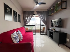 A living room with a red sofa, a television on the wall, a ceiling fan, and a view of the city through large windows. - 1303 · Noble and Modern with garage 1303 (Belém)