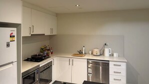 A modern kitchen with white cabinets, a stainless steel dishwasher, and a microwave. - Lunara Hotel (Burwood)