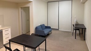 A compact living space with a kitchenette, a dining table, a sofa, and a sliding door closet. - Lunara Hotel (Burwood)