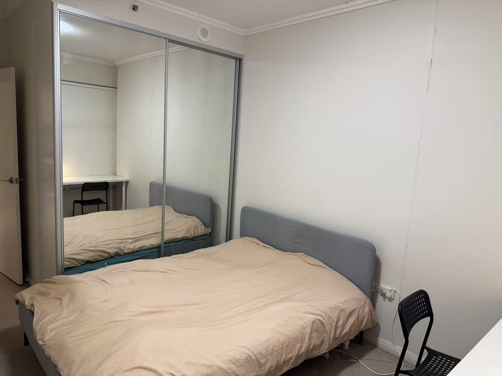 Een slaapkamer met een bed, een stoel, een bureau en een kledingkast met spiegel.