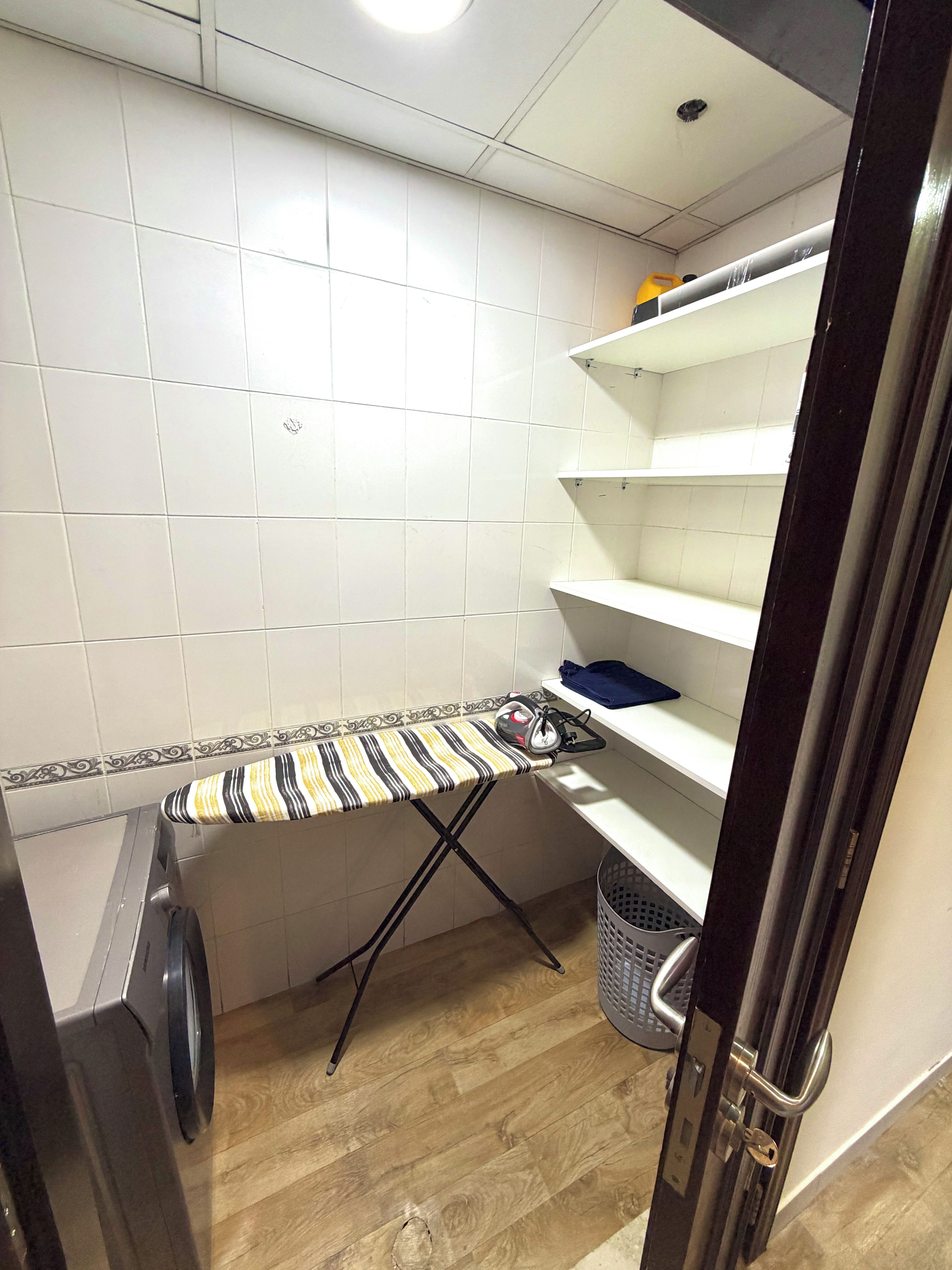 A laundry area with a washing machine, an ironing board, and shelves.