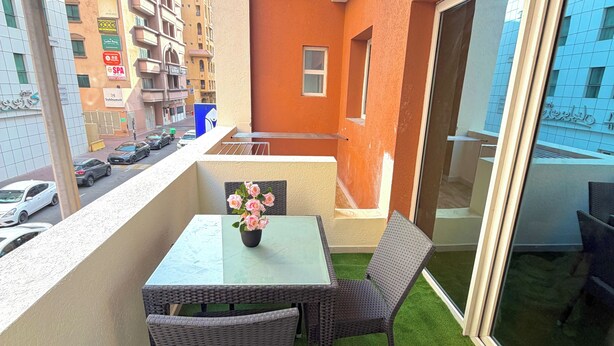Ein Balkon mit Kunstgrasanlage, einem Tisch, Stühlen und einem Blumenstrauß.