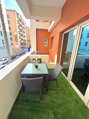 A balcony with artificial grass, a table, chairs, and a vase of flowers. - Homeland Female Hostel (Dubai)