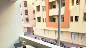 Ein Balkon mit Tisch und Stühlen, einem Kleiderständer und Blick auf ein mehrstöckiges Gebäude mit Balkonen.
