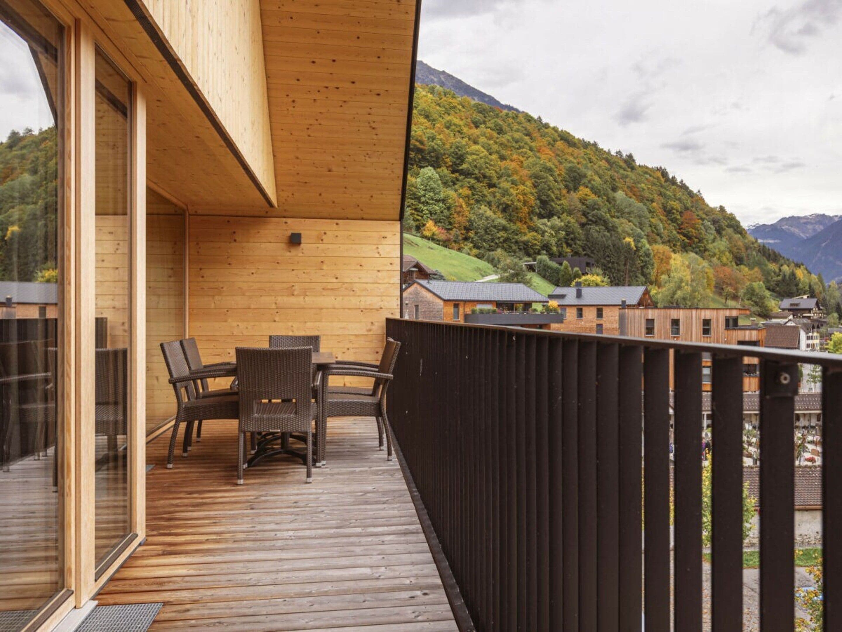 Une terrasse en bois avec une table et des chaises, offrant une vue sur un paysage montagneux.