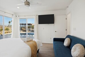 Ein Hotelzimmer mit einem Bett, einem blauen Sofa, einem Fernseher und Blick auf einen Pool.