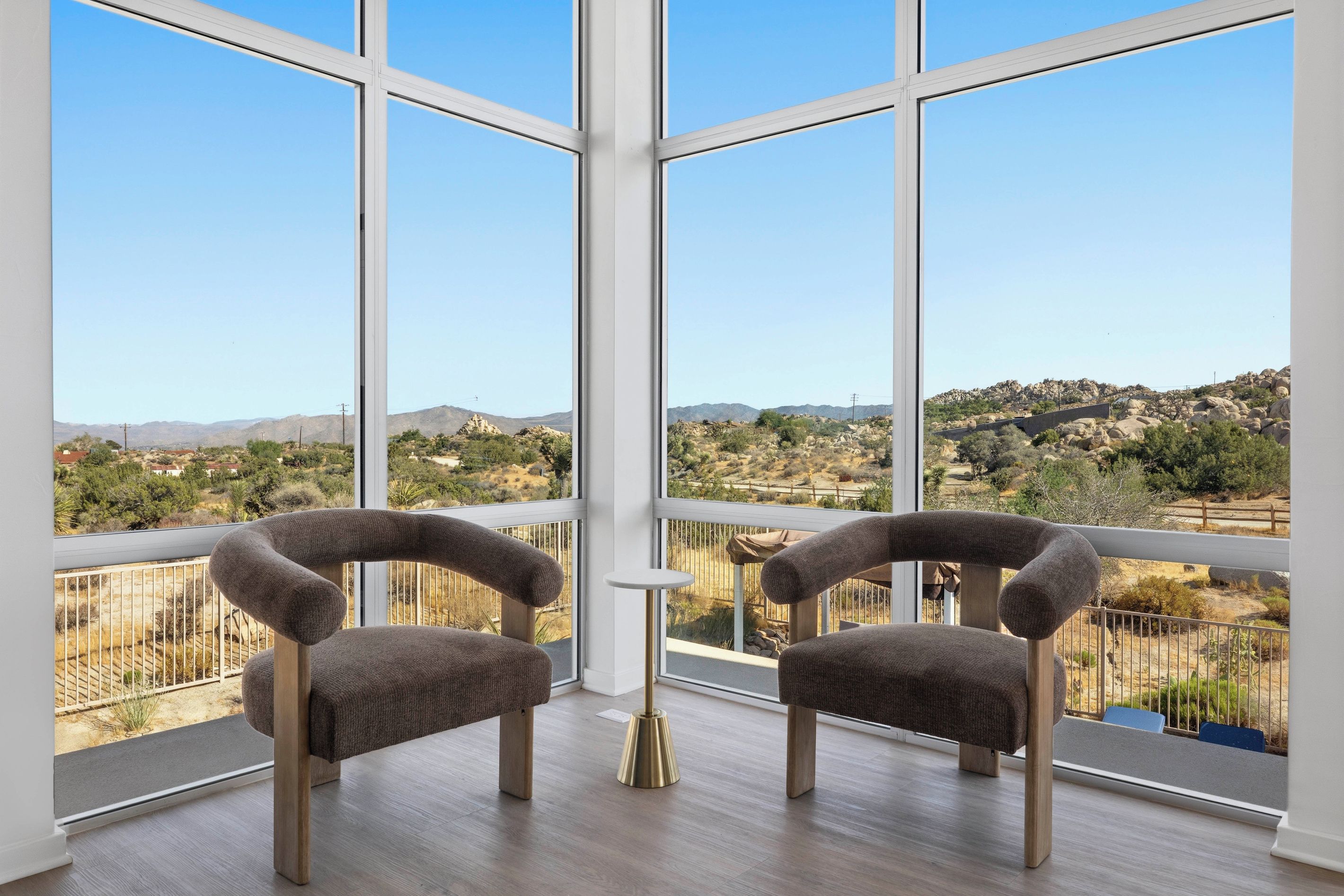 A balcony with two upholstered chairs, a small table, and a view of a hilly landscape.