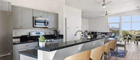 Una cocina moderna con una isla central, taburetes de bar y vistas al exterior.