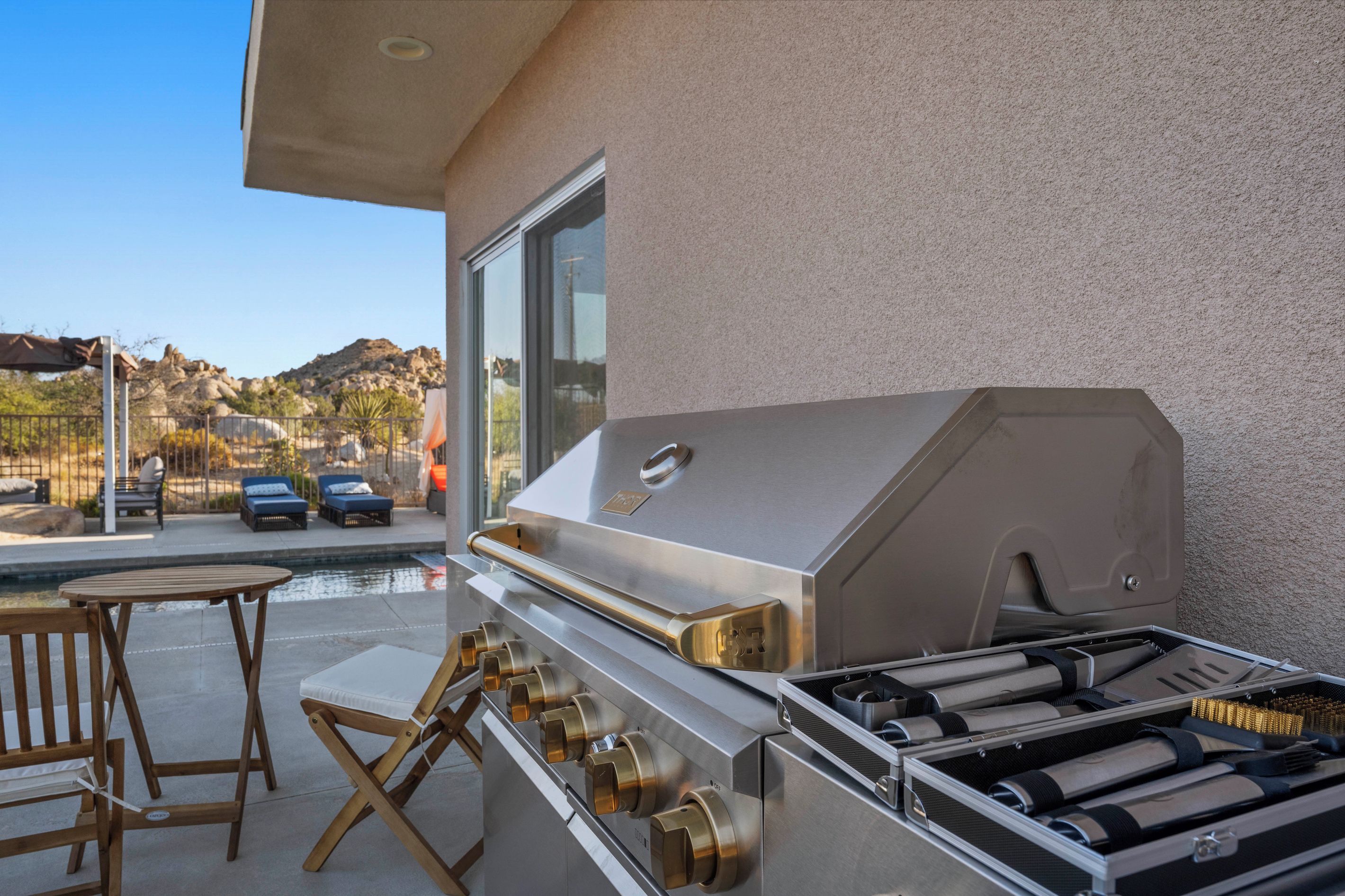 An outdoor grill area with a poolside table and chairs.