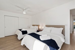 Ein Hotelzimmer mit zwei Betten, einem Deckenventilator, Nachttischlampen und Blick ins Freie.