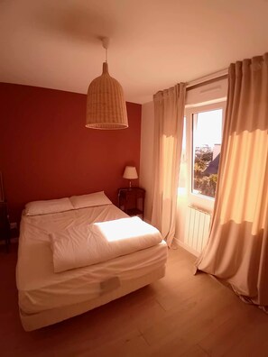 Ein Schlafzimmer mit einem Bett, einem Nachttisch, einer Lampe und einem Fenster mit Vorhängen.