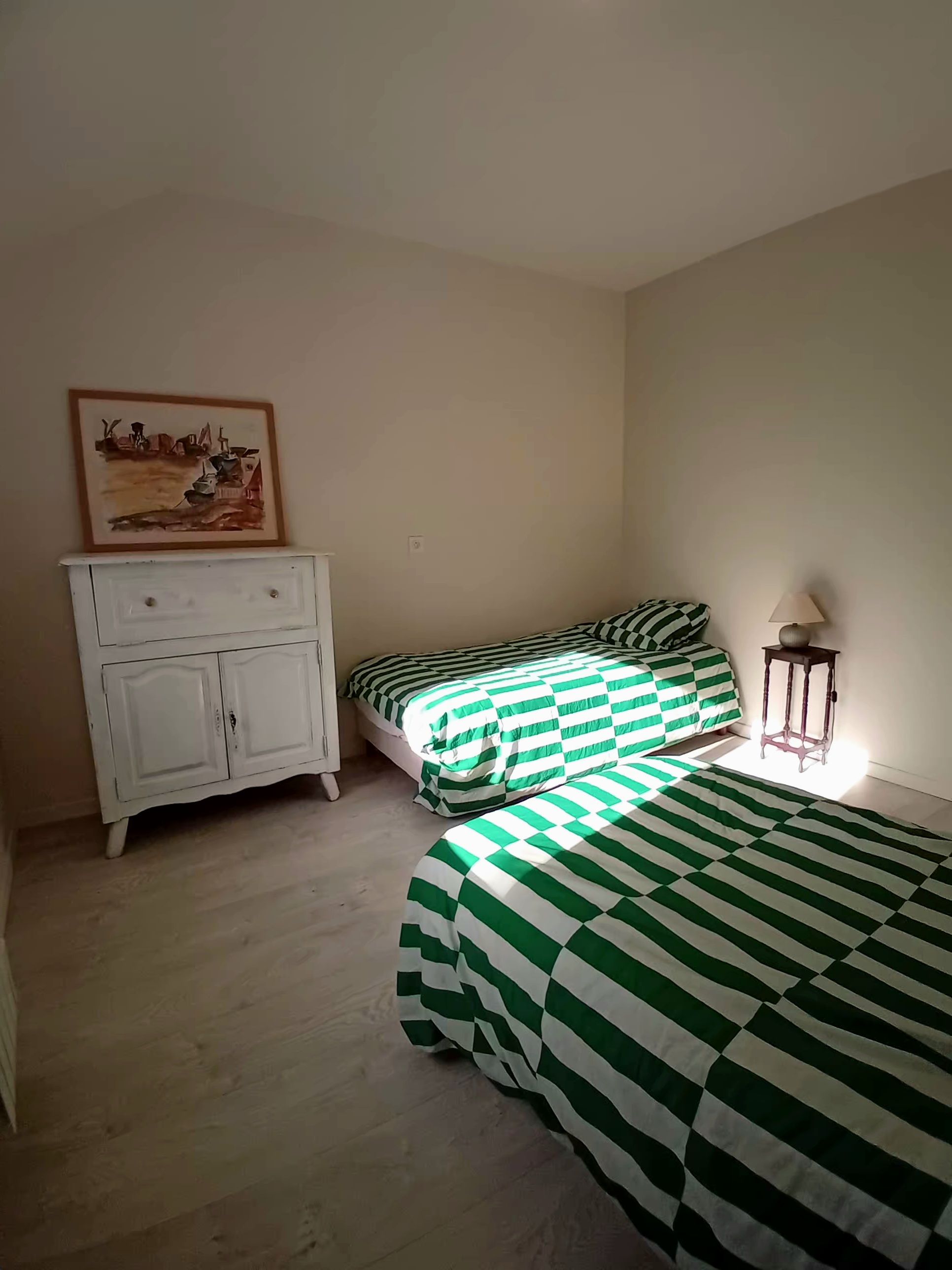 A room with two beds, a white dresser, a lamp, and a painting on the wall.