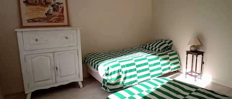 A room with two beds, a white dresser, a lamp, and a painting on the wall.