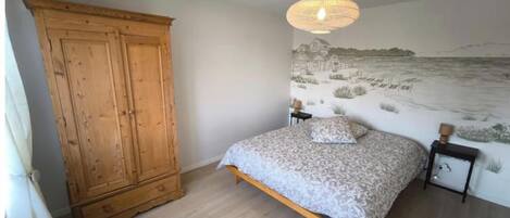 A bedroom with a bed, a wooden wardrobe, a wall mural, and a bedside table with a lamp.