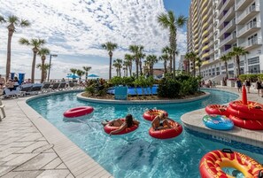 A pool area with multiple inflatable rings, palm trees, and a hotel building in the background. - Oceanfront High‑Rise Condo • Indoor/Outdoor Pools, Lazy River • On the Boardwalk (Daytona Beach)