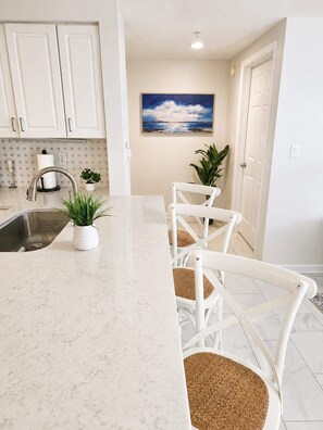 A kitchen with white cabinets, a marble countertop, a sink, and two potted plants. - Oceanfront High‑Rise Condo • Indoor/Outdoor Pools, Lazy River • On the Boardwalk (Daytona Beach)