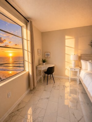 A hotel room with a view of the sunset over the ocean, a desk with a chair, a bedside table with a lamp, and a bed. - Oceanfront High‑Rise Condo • Indoor/Outdoor Pools, Lazy River • On the Boardwalk (Daytona Beach)