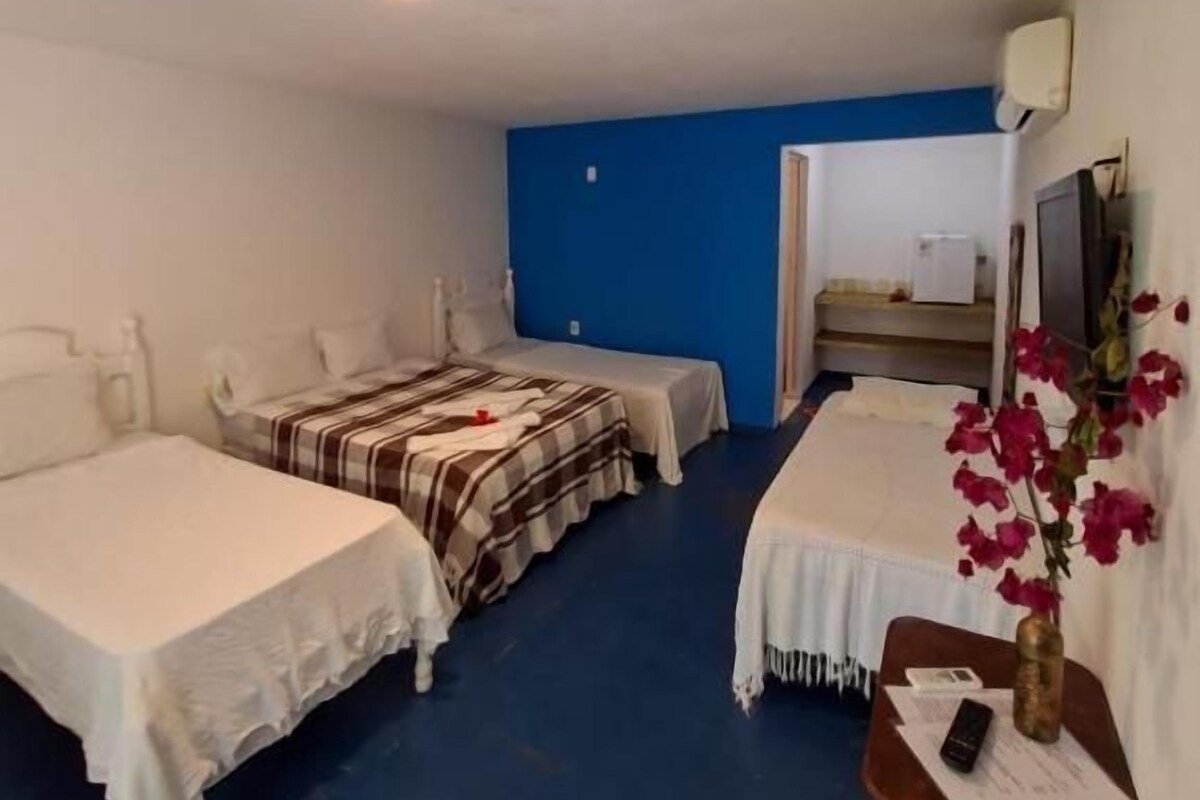 A hotel room with two beds, a desk, a chair, a small table with a vase, and a blue wall.