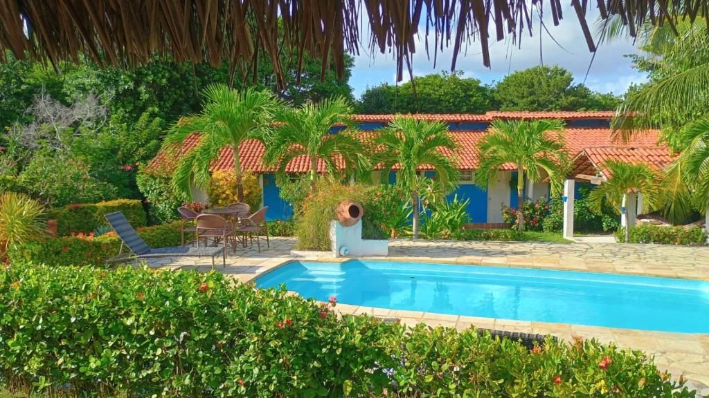 Una piscina rodeada de vegetación exuberante, un patio con sillas y un edificio con tejado de tejas rojas.