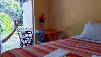 Habitación de hotel con cama, una mesita, una silla y una hamaca fuera de la ventana.