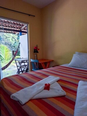 A hotel room with a bed, a small table, a chair, and a hammock outside the window. - Pousada dos Mundos (Conde)