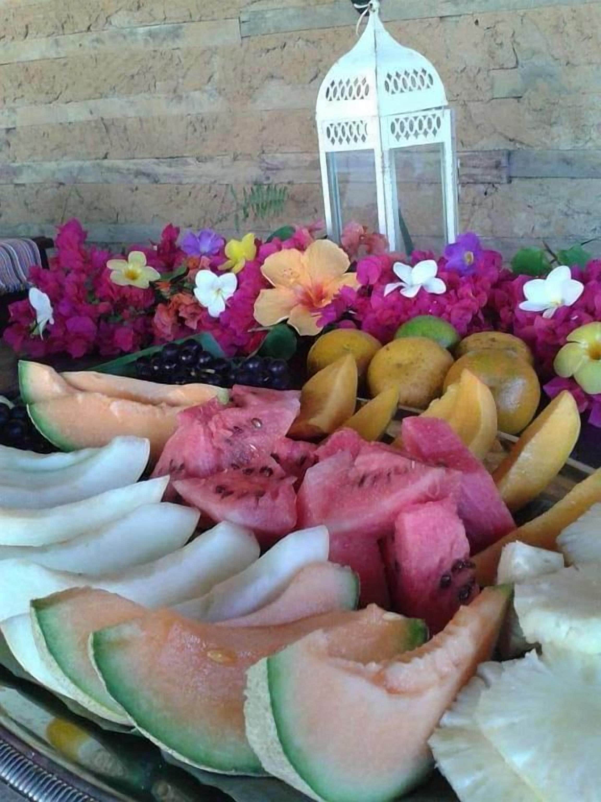 Una exhibición de frutas y flores con un farol al fondo.