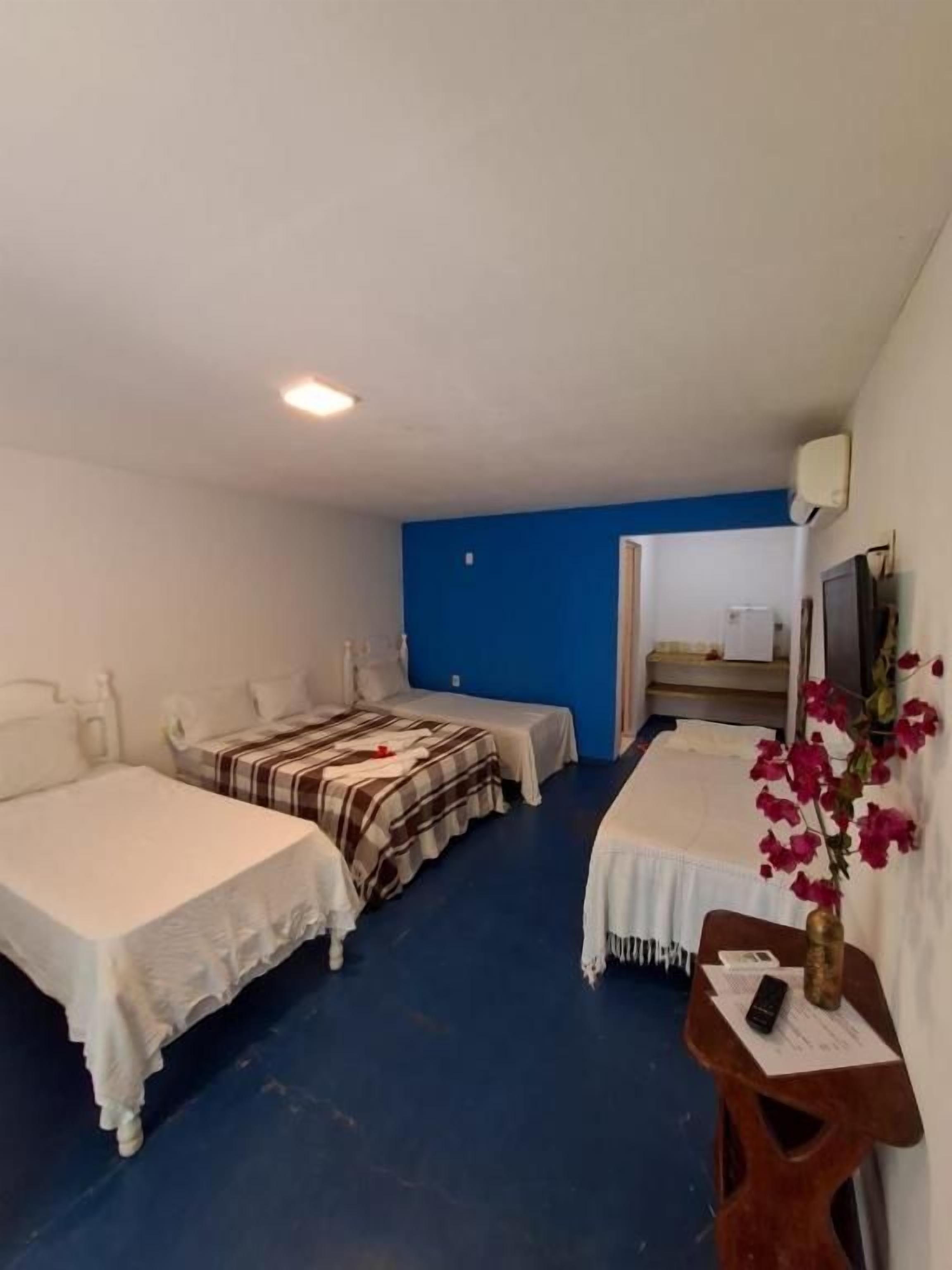 Habitación de hotel con dos camas, un escritorio, una silla, una mesita con un florero y una pared azul.