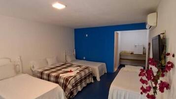 Habitación de hotel con dos camas, un escritorio, una silla, una mesita con un florero y una pared azul.