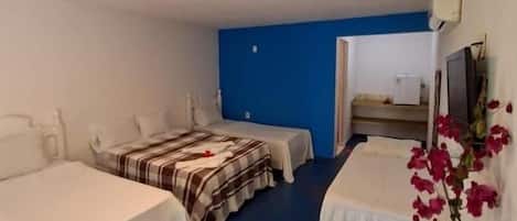 A hotel room with two beds, a desk, a chair, a small table with a vase, and a blue wall.