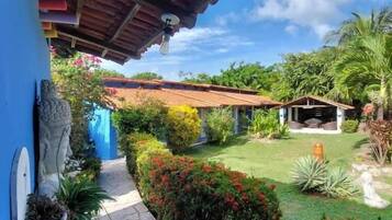 A pathway leading to a house with a red-tiled roof, surrounded by a garden with various plants and a clear sky.
