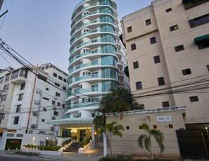 Et moderne hotel med en buet facade, flere altaner og en godt oplyst indgang.