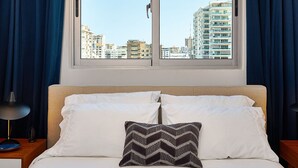 Ett hotellrum med en säng, ett fönster med gardiner och utsikt över stadens byggnader.
