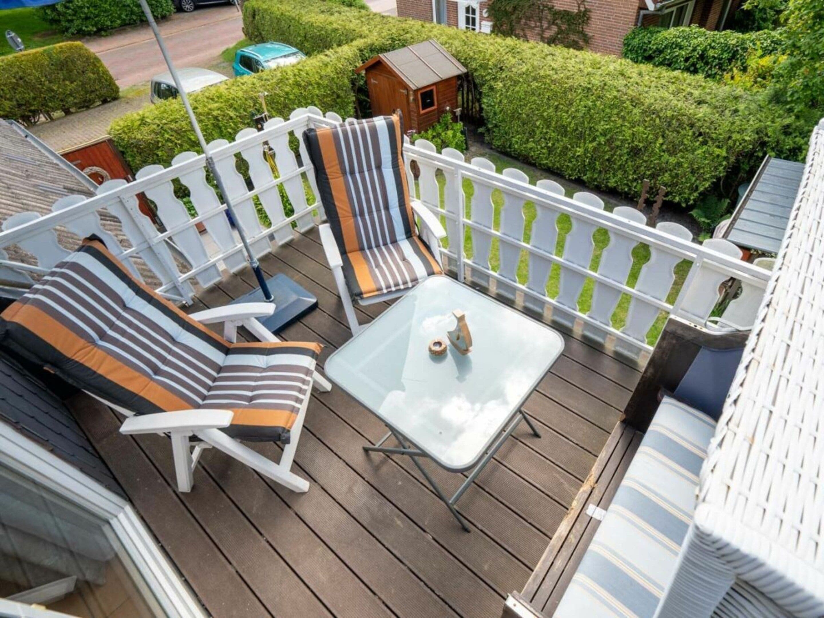 A deck with two lounge chairs and a small table, surrounded by a white picket fence.