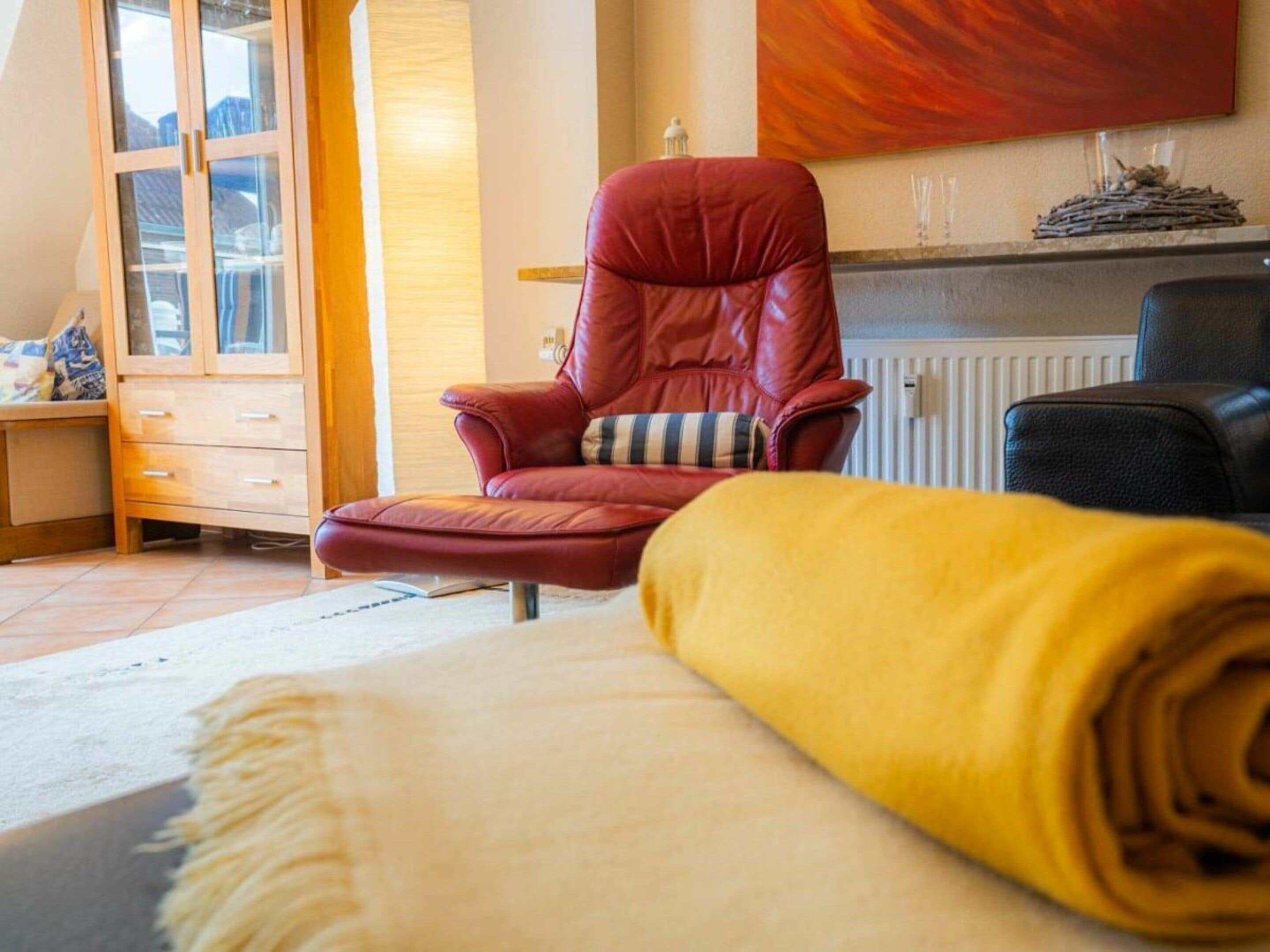 A room with a red leather chair, a yellow rolled-up blanket, a wooden cabinet with glass doors, and a radiator.