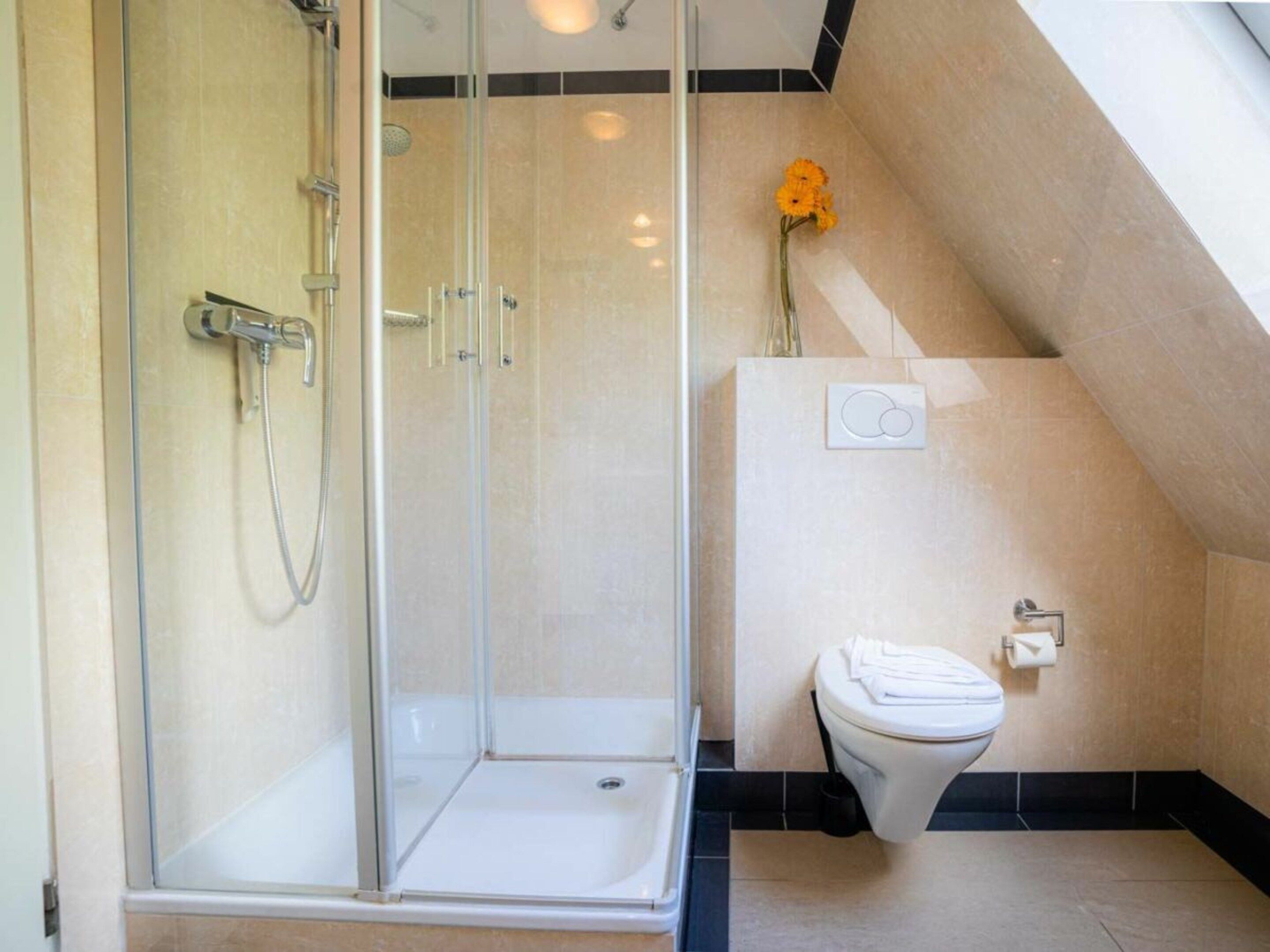 Une salle de bain moderne avec une douche à parois de verre, des toilettes et un petit arrangement floral.