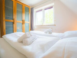Ein Hotelzimmer mit zwei Betten, einem Holzschrank mit Glastüren, einem Fenster mit Vorhängen und einer Heizung.
