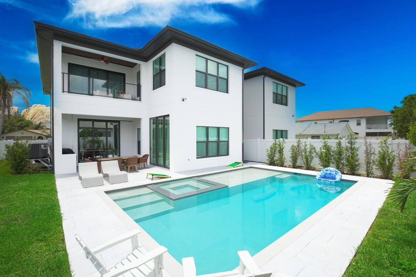 A modern two-story house with a swimming pool, outdoor furniture, and a clear blue sky.