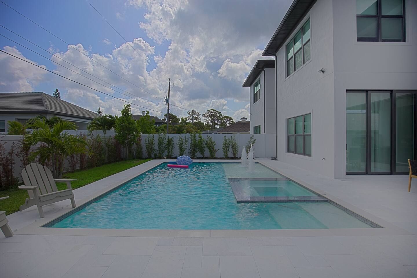 A modern residential swimming pool with a clear sky and a white house in the background.