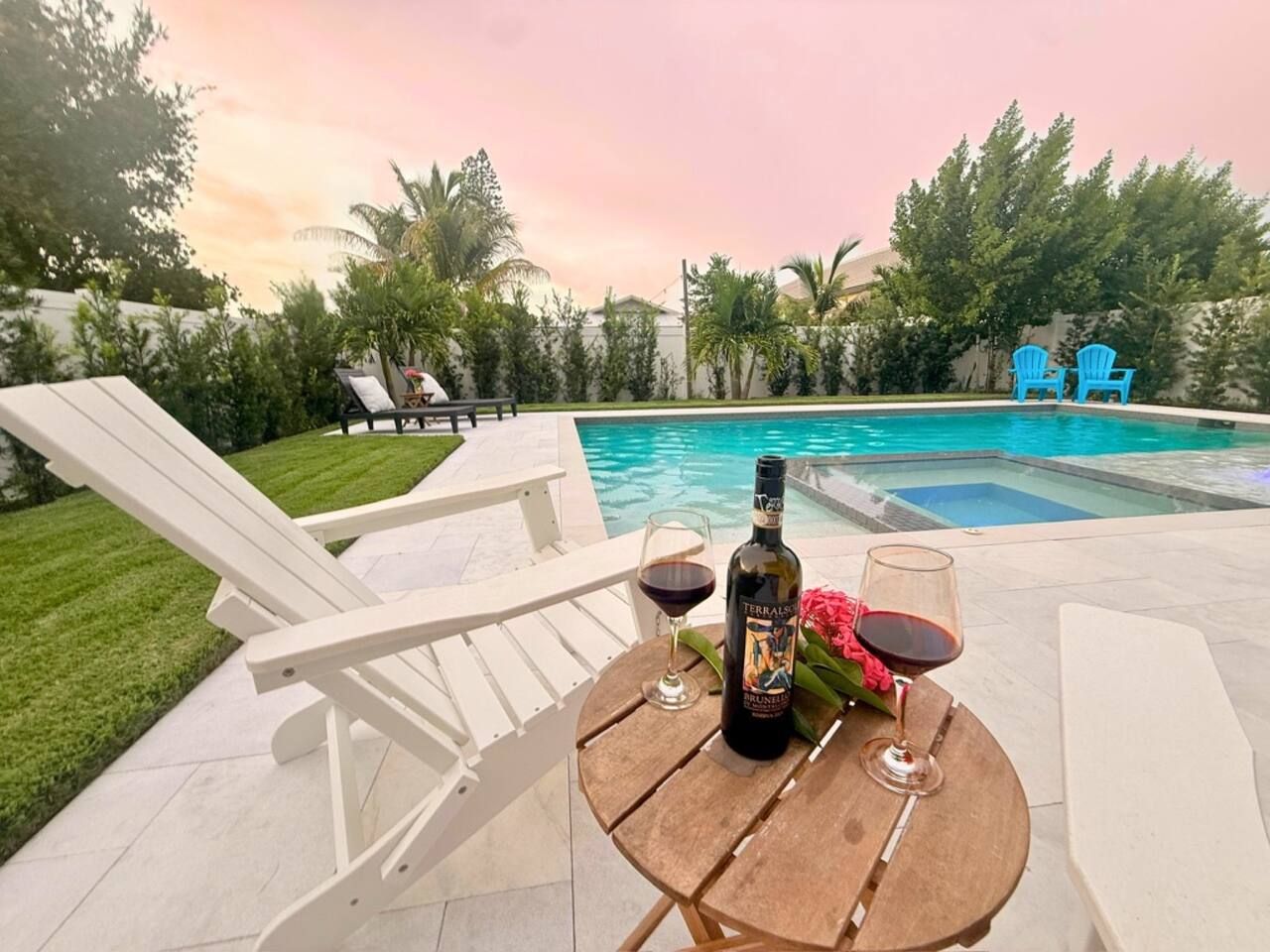 Escena junto a la piscina con una mesa, dos sillones reclinables, una botella de vino y copas.