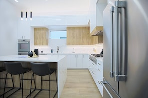 A modern kitchen with a central island, bar stools, a built-in oven, and a stainless steel refrigerator. - *New* Naples Villa w/ Pool Jacuzzi | Sleeps 14 (Naples)