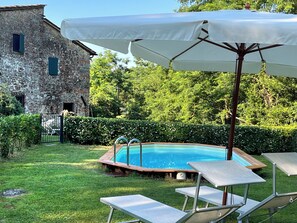 Une piscine dotée d’une terrasse en bois, entourée d’une pelouse agrémentée d’un parasol blanc et de chaises longues.