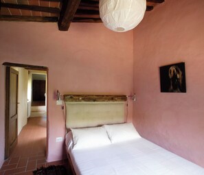 A bedroom with a wooden headboard, a bed with white bedding, a hanging light fixture, and a painting on the wall. - Villa in Tuscany, private pool, Wi-Fi, parking, pet-friendly, in the woods (Toscana)