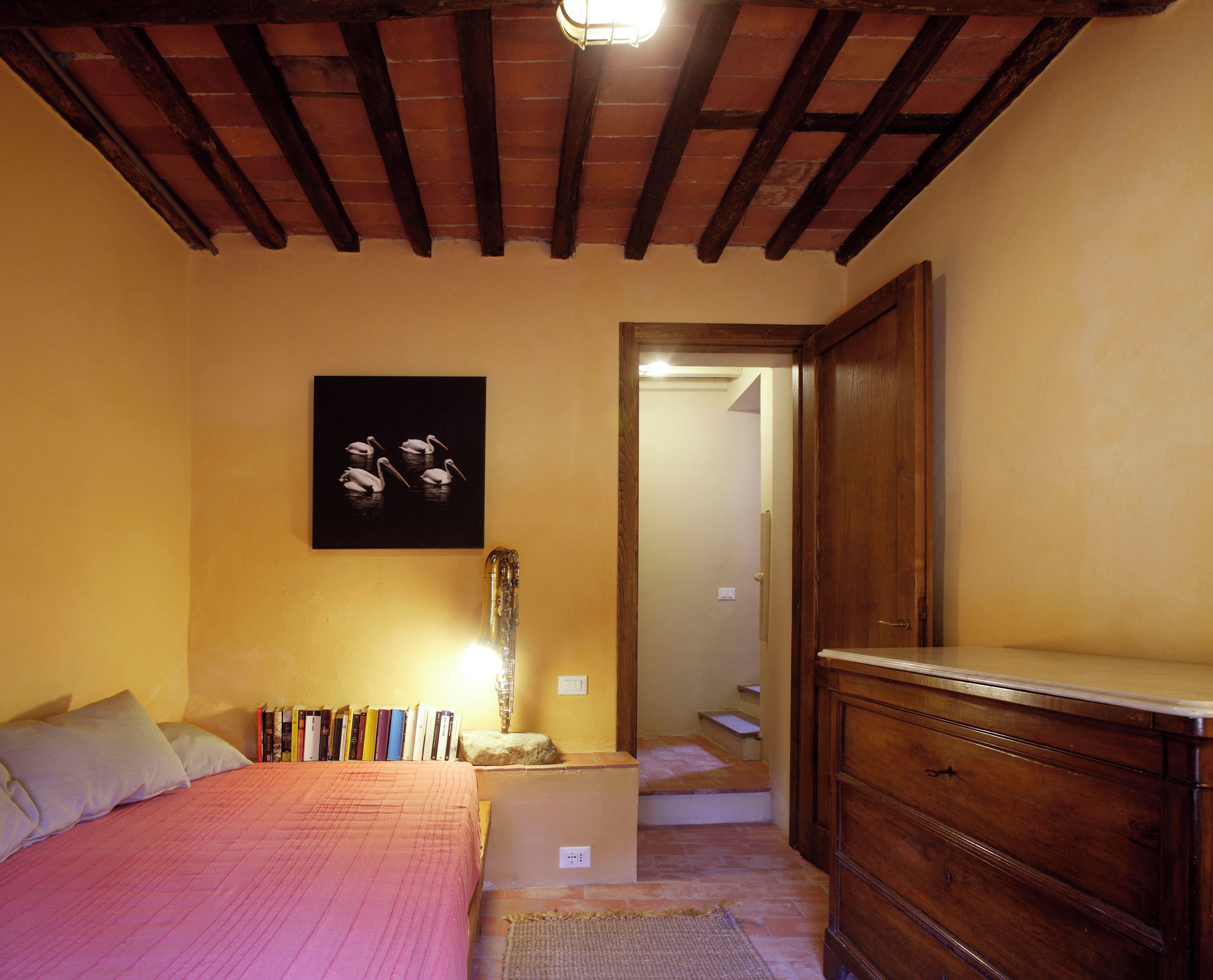 A bedroom with a bed, a wooden dresser, a bookshelf, and a framed picture on the wall.