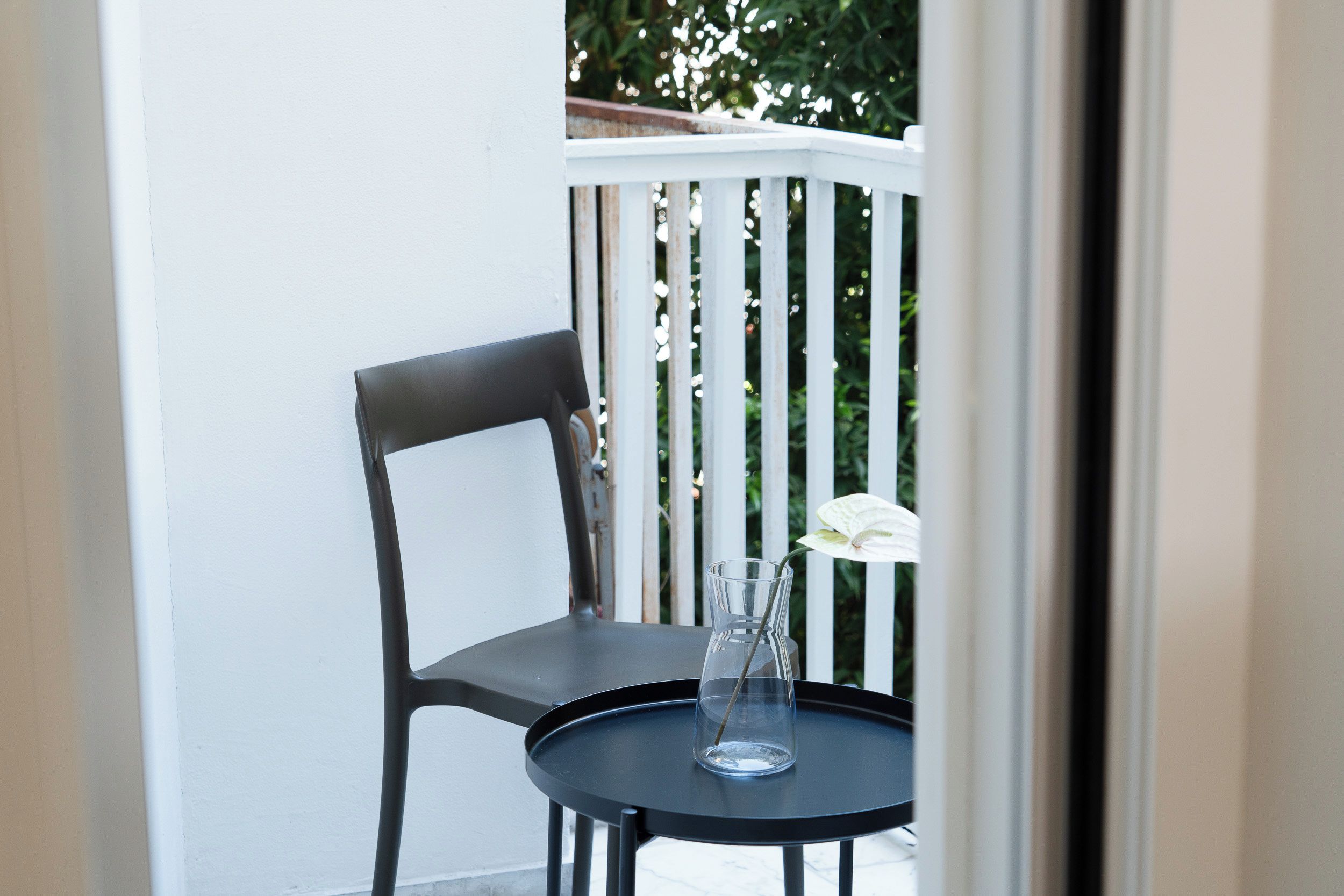 Een balkon met een zwarte stoel en een kleine ronde tafel met een glazen vaas met daarin een enkele witte bloem.