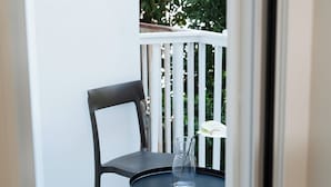 Un balcone con una sedia nera e un tavolino rotondo con un vaso di vetro trasparente contenente un singolo fiore bianco.