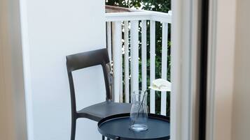 Een balkon met een zwarte stoel en een kleine ronde tafel met een glazen vaas met daarin een enkele witte bloem.