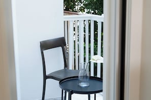 Een balkon met een zwarte stoel en een kleine ronde tafel met een glazen vaas met daarin een enkele witte bloem.