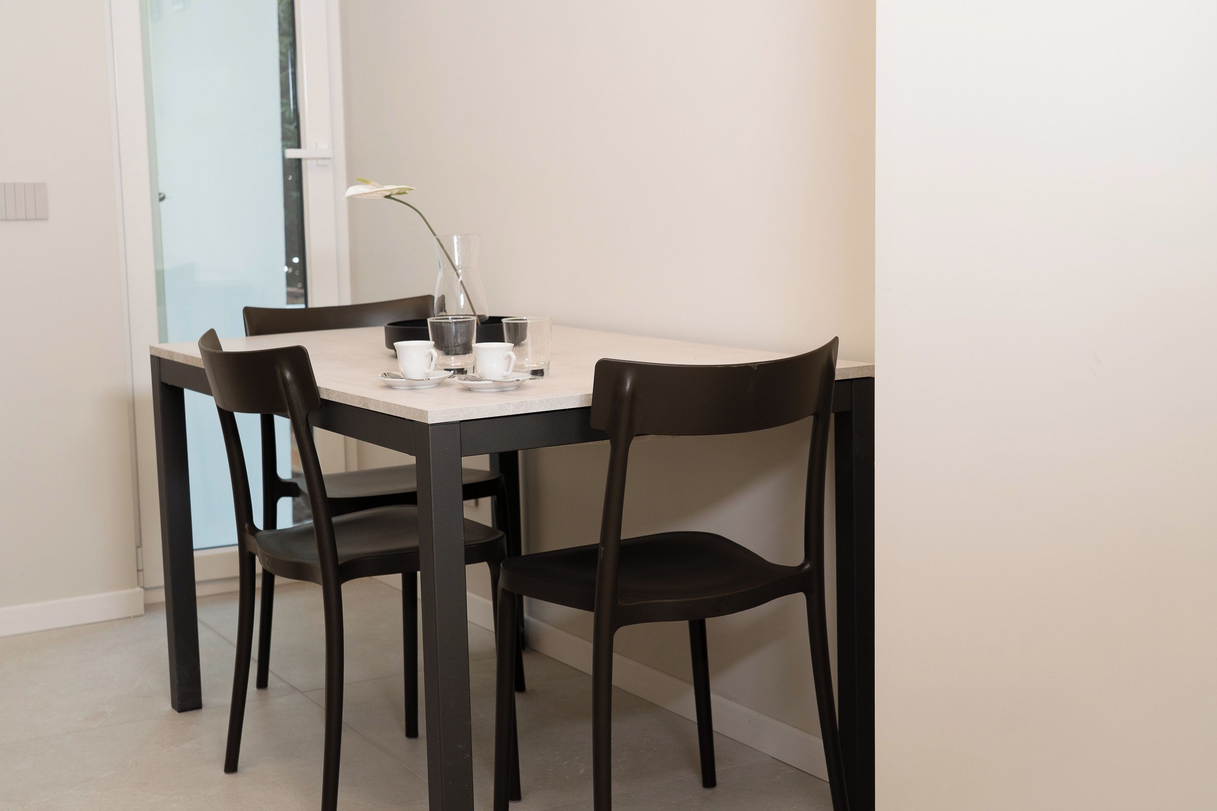 Una mesa de comedor con cuatro sillas, una jarrón de vidrio y dos tazas.