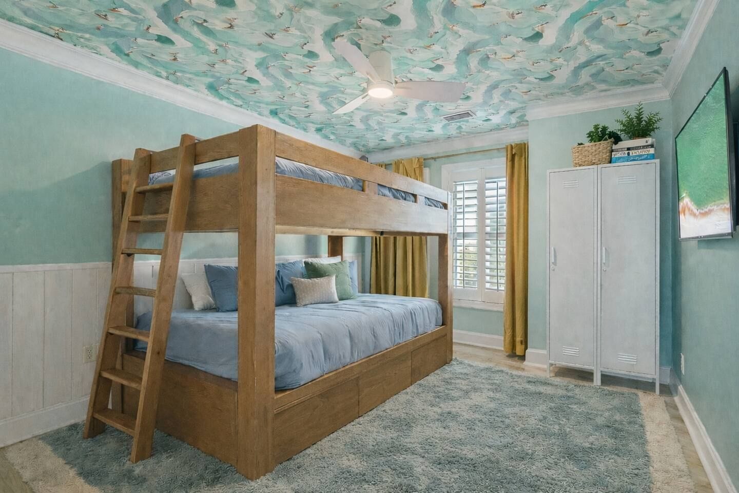 A bunk bed with a ladder, a ceiling fan, a window with curtains, and a wardrobe.